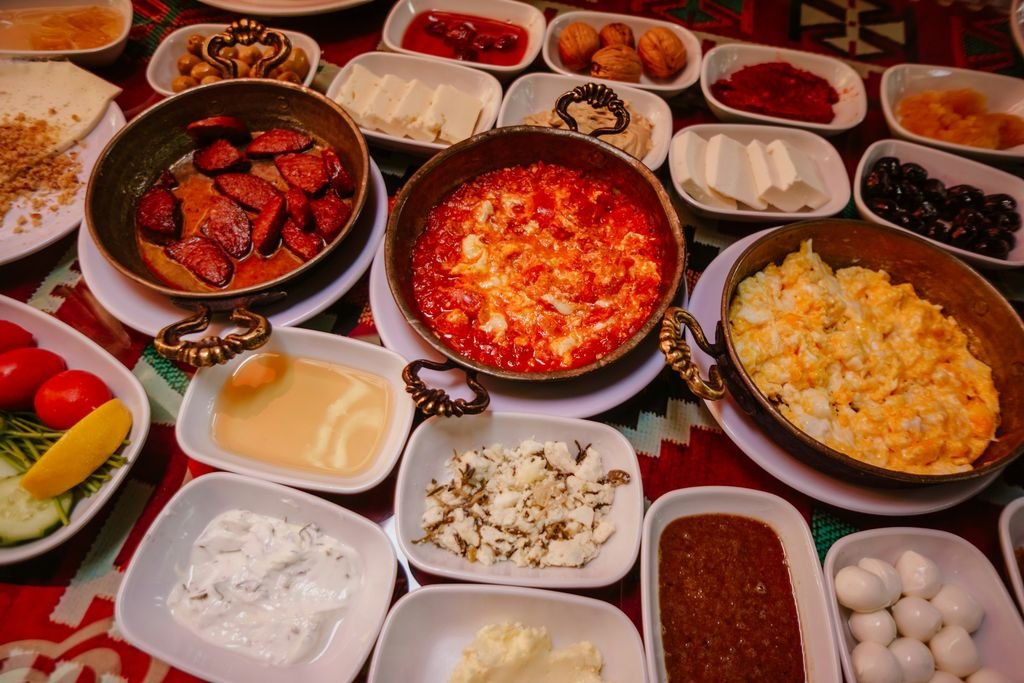Menemen, sucuk, peynir ve zeytin tabaklarıyla dolu bir serpme kahvaltı sofrası