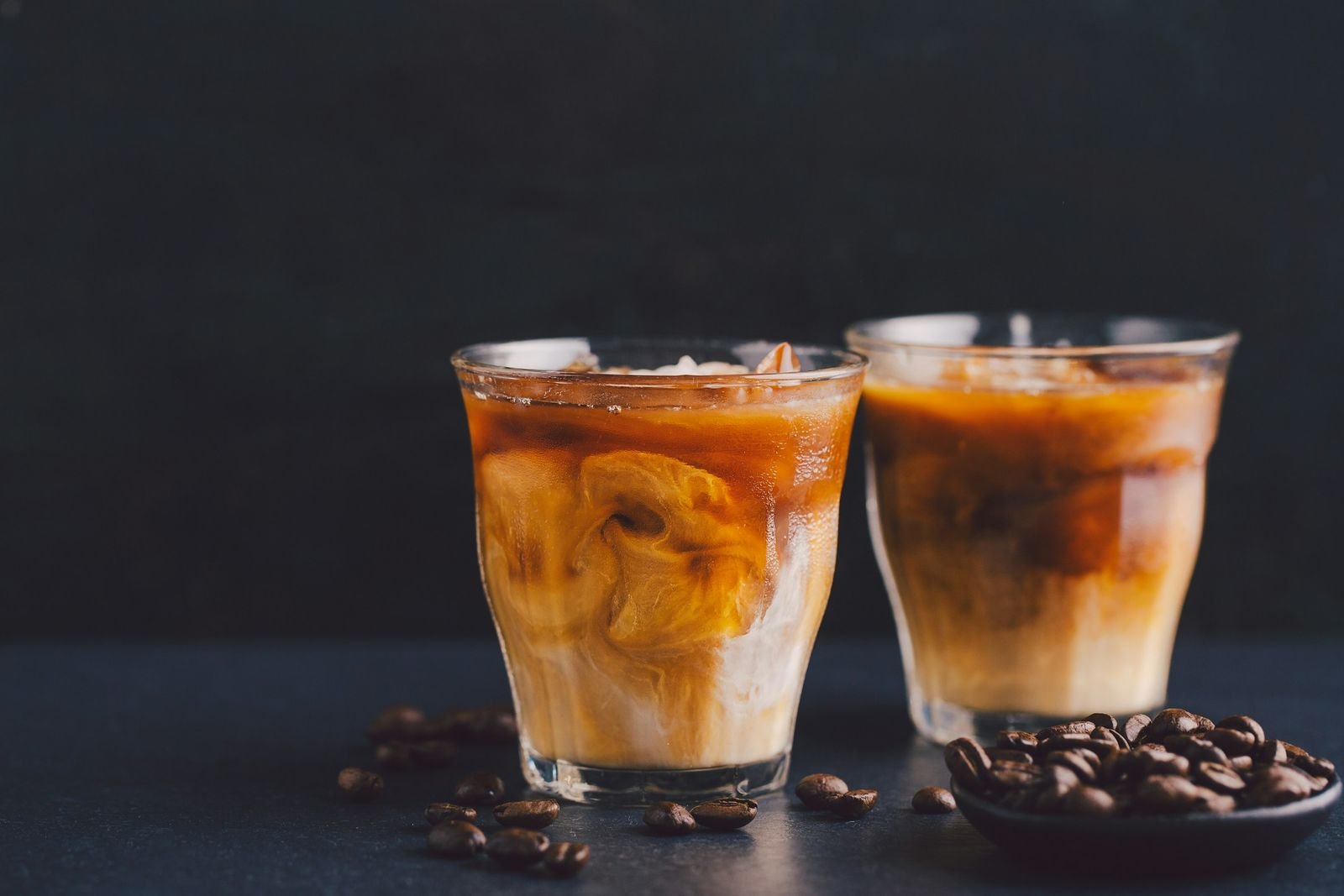 Koyu zemin üzerinde buzlu iki bardak soğuk latte