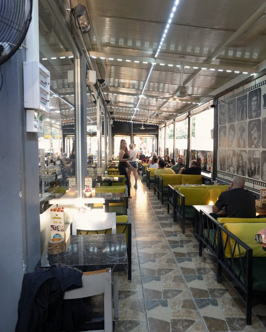 Sarı minderli koltuklar ve masalarla uzanan, üstü kapalı teras